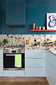 Weißer Küchenzeile, Arbeitsplatte und Spritzschutz aus Marmorterrazzo, darüber Regal an blauer Wand
