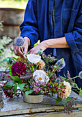 Arranging a flower arrangement with dahlias, globe thistle, heather and poppy capsules