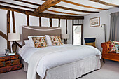 Double bed and vintage suitcase collection in white bedroom with rustic wooden beams