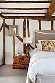 Double bed and vintage suitcase collection in white bedroom with rustic wooden beams