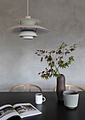 Dining table with black tabletop, vase, dishes, and book, classic pendant light above it