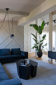 Eleganter Wohnraum mit dunkler Sofagarnitur, schwarzem Couchtisch, Pendelleuchte und Zimmerpflanze