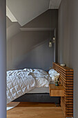 Double bed with wooden headboard and integrated bedside table in the bedroom with grey walls