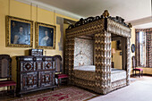 Four postered bed with 17th century flame stitch embroidery and gilt framed artwork above inlaid cabinet