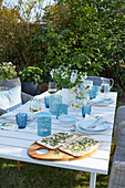 Gedeckter Tisch mit Gläsern und Windlichtern in Blautönen im Garten