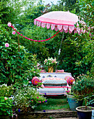 Parasol over garden table with bouquet of flowers and bench with colourful cushions