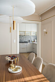 Dining space in a living room, beige pastel colours and brass and golden details, dining table, kitchen with stone worktop and wall