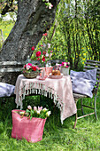 Gartentisch mit Frühlingsblumen und Gugelhupf, Tasche mit Tulpen im Gras