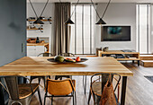 Dining table, industrial chairs and lamps above the table, TV corner in the background