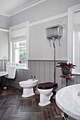 Toilet with nickel finish cistern and bidet in the bathroom with wood-look floor tiles