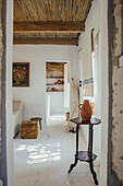 Side table with jug in whitewashed room with bamboo ceiling