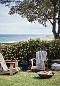 Wooden chairs in front of flowering hedge with sea view