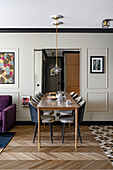 Walnut table with velvet upholstered chairs in black and beige, large wall mirror and herringbone parquet flooring