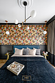 Double bed with blue velvet headboard, wallpaper with tropical pattern on the wall