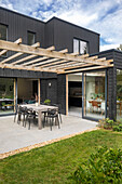 Terrace with pergola and dining table in front of house with black façade