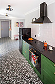 Dark green base units with black conglomerate worktop and geometric floor tiles in open-plan kitchen
