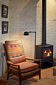 Reading chair next to wood stove in front of rustic brick wall