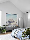 Bright bedroom with sloping ceiling, mirror, plants, lowboard, artwork above