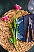 Place setting with seagrass place mat, blue ceramic plate, and tulips (Tulipa)
