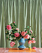 Rosen in blauer Vase vor grün-kariertem Vorhang
