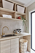 Modern Scandi style laundry room with custom made beech wood cabinets and shelves, and golden faucet