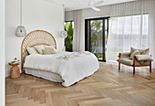 Bright bedroom with cane headboard, oak parquet flooring, and tropical garden view