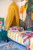 Kinderzimmer mit Betthimmel, floraler Tapete und farbenfrohen Akzenten