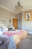 Schlafzimmer mit Kronleuchter, Bildern und rosafarbenem Fell auf dem Bett