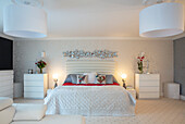 Brightly designed bedroom with double bed, many chests of drawers and large lamps