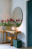 Round wall mirror, decoration with red flowers and candles on antique wooden bench