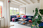 Living room with blue corner sofa, colorful throw pillows and monstera