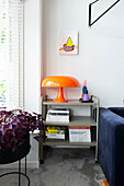 Shelf with books and orange lamp next to blue sofa