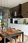 Dining area with industrial wooden table and patterned wallpaper in the kitchen