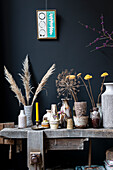 Rustikale Werkbank dekoriert mit Trockenblumen und Keramikvasen vor schwarzer Wand