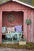 Gartenhütte dekoriert mit Kränzen, Kissen und Decke