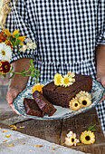 Person hält Teller mit Schokoladenkuchen und Blumen-Dekoration