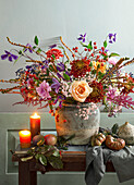 Autumn bouquet in a stone vessel surrounded by apples, tomatoes and burning candles