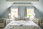 Bedroom with sloping ceilings, light blue walls and bed with floral bed linen