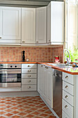 Kitchen with white cupboards, terracotta tiles on the wall and floor