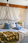 Bed with patterned and plain-coloured cushions, wire pendant light