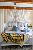 Bed with patterned bedspread and pendant light in bedroom with ceiling beams