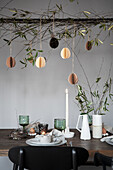 Easter decoration with hanging paper eggs and olive branches above a laid table