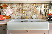 Ceramic sink with gold tap in kitchen with mosaic tiled splashback