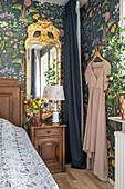 Bedroom with floral wallpaper, wooden furniture and dress on hanger