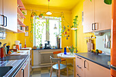 Rosa Schränke und Frühstückstisch in Küche mit gelben Wänden