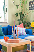 Kerzen auf Couchtisch aus weißem Kunststoff, dahinter blaues Sofa und Zimmerpflanzen