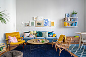 Living room with blue sofa, yellow armchair, rattan armchairs, pictures, shelf and colourful cushions