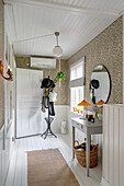 Hallway with patterned wallpaper and white floorboards, coat rack and console table