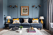 Klassisches Wohnzimmer mit blauen Wänden, farblich passendem Samtsofa und gelben Akzenten