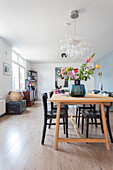 Bright dining room with wooden table, bouquet of flowers and modern lamp